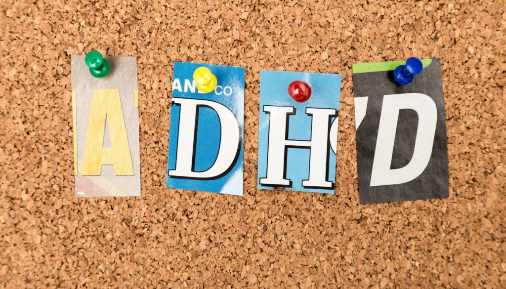 Letters "adhd" cut out from various printed materials and pinned to a corkboard.