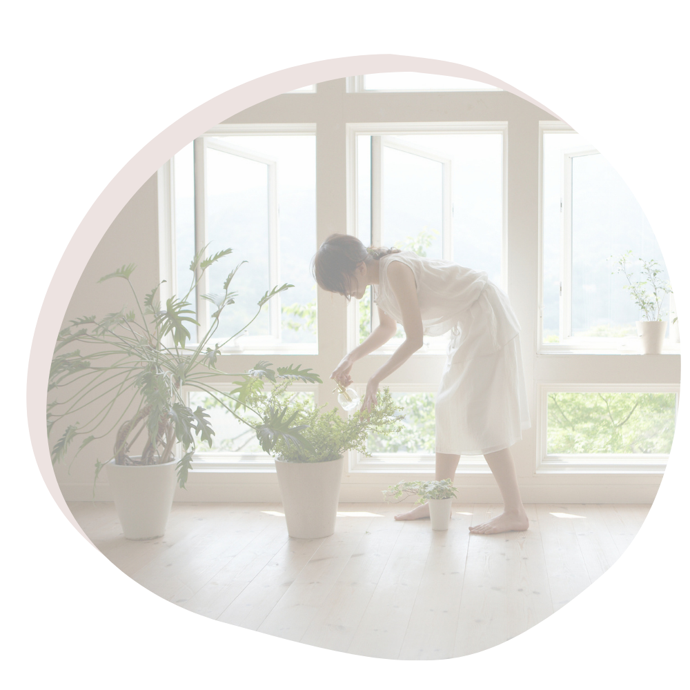 A person in a white dress tenderly tending to plants in a bright, sunlit room.